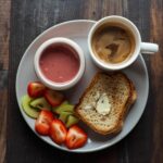 Un petit-déjeuner équilibré avec smoothie et fruits tranchés, un café avec un nuage de lait, du pain grillé avec du beurre